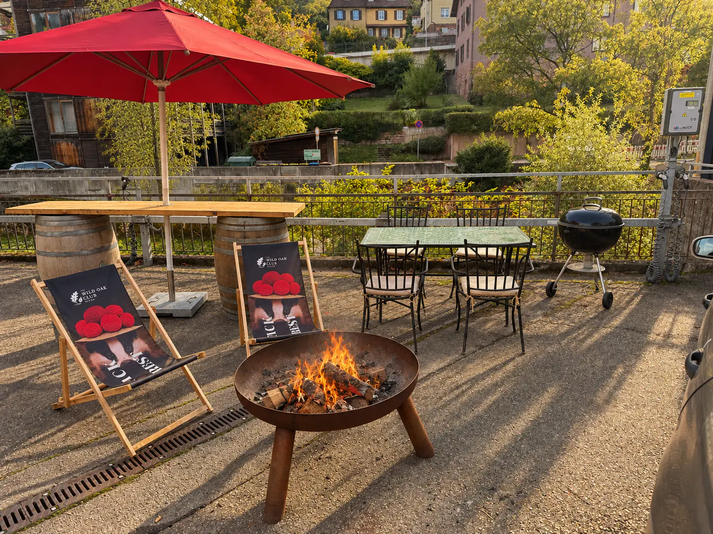 Außenbereich mit brennender Feuerschale, Liegestühlen, Grill und roten Sonnenschirmen