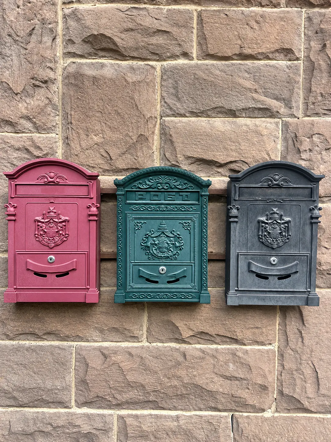 Drei historische Briefkästen in Rot, Grün und Schwarz an der Sandsteinwand der Alten Post
